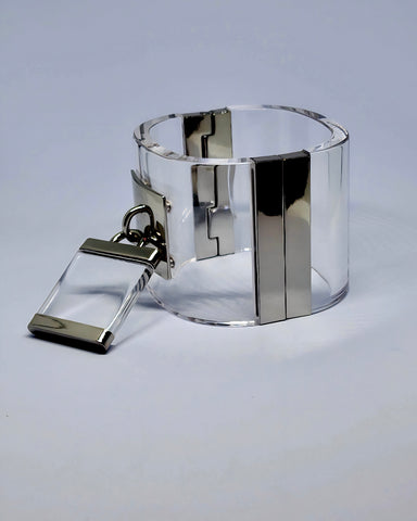 The Drop Lock Silver Lucite Bangle Bracelet from Nik Spruill showcases silver metallic accents and a matching rectangular charm, elegantly secured with a magnetic closure.