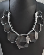 The Tribal Liquid Lucite Sculptural Necklace by Nik Spruill features large, faceted, clear geometric beads strung together on a black cord, displayed against a black background. This sculptural piece epitomizes modern luxury.