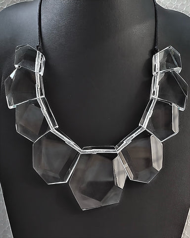 The Tribal Liquid Lucite Sculptural Necklace by Nik Spruill features large, faceted, clear geometric beads strung together on a black cord, displayed against a black background. This sculptural piece epitomizes modern luxury.