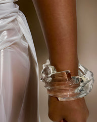 Close-up of an arm adorned with the Nik Spruill Spiral Liquid Lucite Cuff Bracelet. The person is wearing a silky white garment tied at the waist.
