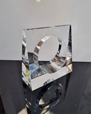 The Liquid Lucite Wedge Bangle Bracelet by Nik Spruill, a clear, geometric masterpiece with a distinctive circular opening at its center, is displayed on a reflective black surface against a neutral backdrop, radiating an elegance akin to sophisticated jewelry.