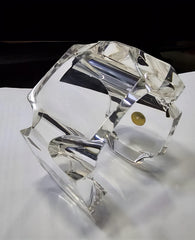 A close-up of the Nik Spruill Liquid Lucite Infinity Cuff Bracelet, showcasing its hand-sculpted faceted design with angular cuts that reflect light beautifully. Placed on a plain surface, the high-quality lucite craftsmanship enhances both its elegance and allure.