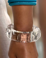 Close-up of a wrist wearing a sophisticated piece: the Nik Spruill Link Lucite Unisex Tennis Cuff Bracelet, featuring a large, faceted clear design. The background is blurred, highlighting this modern tennis bracelet.