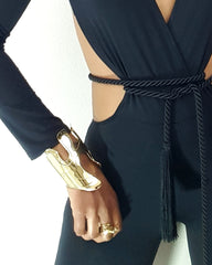 A woman wearing an OSHUN black jumpsuit with a gold belt around her waist by Nik Spruill.