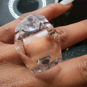 A woman's hand holding a clear YIZ ring by Nik Spruill.