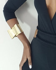 A woman wearing an ASHANTI black dress and a Nik Spruill gold bracelet.