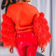 model in a red neoprene top with feather sleeve and back zipper back view with red patent pants