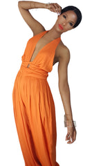 A woman in a Nik Spruill fearless one deep plunge backless jumpsuit - orange, posing for a picture.