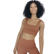 A person with curly hair wears the Nik Spruill SHIVAYA CROP TOP, a brown sleeveless crop top paired with pants made from 4-way stretch fabric, set against a white background.